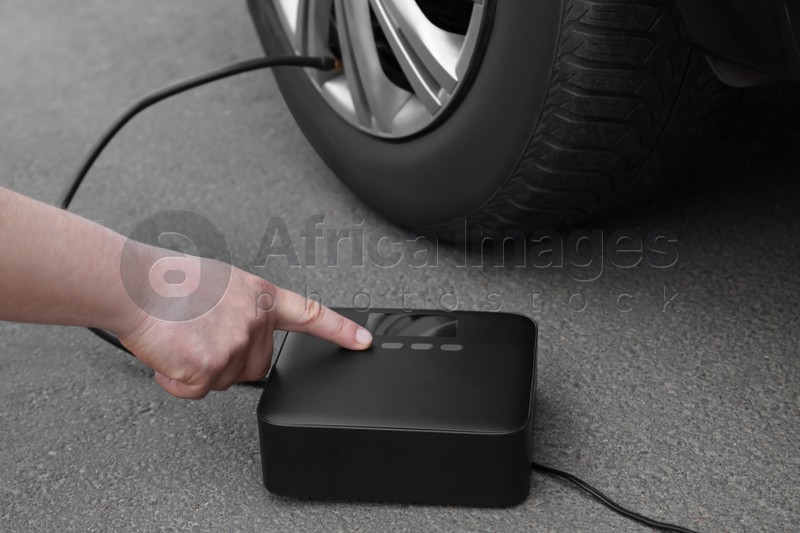 Photo of Man using portable air pump to inflate car tire outdoors, closeup