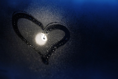 Glass with heart drawn in condensation against dark background. Space for text