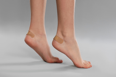 Girl showing feet with sticking plasters on light grey background, closeup