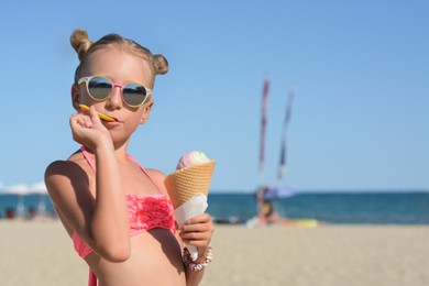 Adorable little girl in swimsuit with delicious ice cream at beach on sunny summer day, space for text