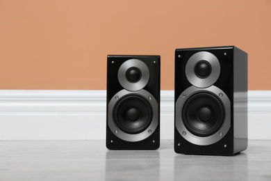Modern powerful audio speakers on floor near orange wall