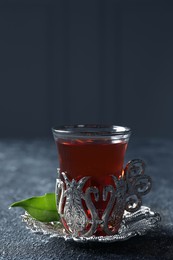 Photo of Glass of traditional Turkish tea in vintage holder on grey textured table