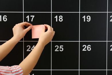 Photo of Woman putting sticker on board calendar, closeup