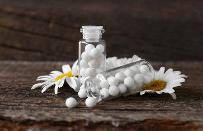 Bottles with homeopathic remedy and flowers on wooden table, closeup