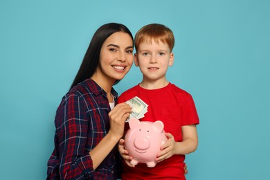 Mother and her son putting money into piggy bank on light blue background