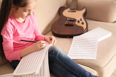 Little girl with guitar writing music notes at home
