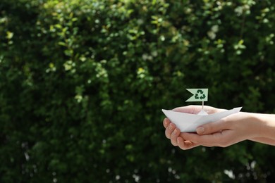Photo of Woman holding paper boat with recycling symbol outdoors, closeup. Space for text