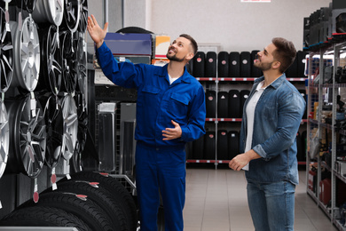 Photo of Male mechanic helping client to choose alloy wheel in auto store