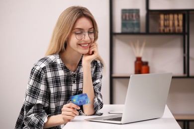 Woman with credit card using laptop for online shopping at white table indoors