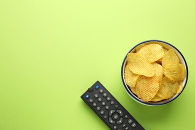 Remote control and bowl of potato chips on light green background, flat lay. Space for text
