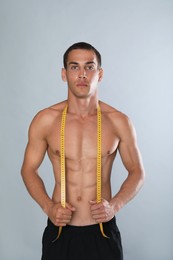 Handsome shirtless man with slim body and measuring tape on grey background