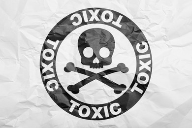 Hazard warning sign (skull-and-crossbones symbol and word TOXIC) on crumpled white paper, top view