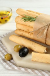 Tasty grissini with rosemary, olives and oil on white wooden table, closeup