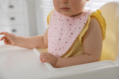 Cute little baby wearing bib in highchair indoors, closeup