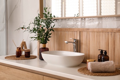 Photo of Vase with beautiful branches, candles and air reed freshener near vessel sink in bathroom. Interior design