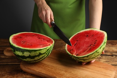Woman cutting delicious watermelon at wooden table against dark grey background, closeup