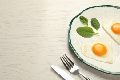 Heart shaped fried eggs served on white wooden table, space for text