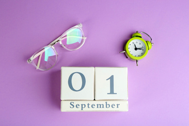 Calendar, glasses and alarm clock on violet background, flat lay