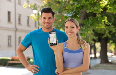 Couple showing smartphone with fitness app outdoors, focus on device