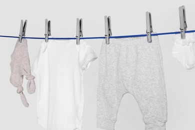 Different baby clothes drying on laundry line against light background, closeup