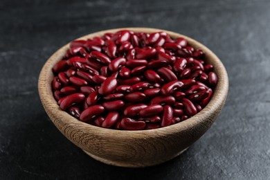 Raw red kidney beans in wooden bowl on black table, closeup