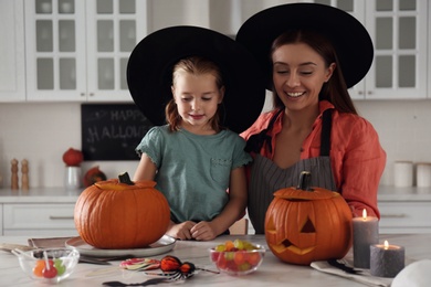 Mother and daughter making pumpkin jack o'lanterns at table in kitchen. Halloween celebration