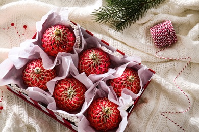 Beautiful red Christmas baubles in box on knitted plaid, flat lay