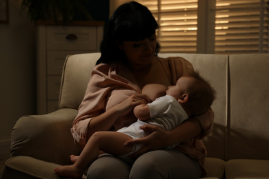 Woman breastfeeding her little baby on sofa in evening