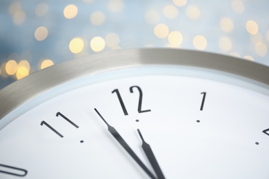 Clock on light blue background with blurred lights, closeup. New Year countdown