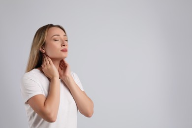 Young woman doing thyroid self examination on light grey background, space for text