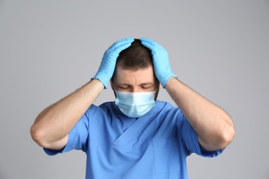 Stressed doctor in protective mask on grey background. Mental health problems during COVID-19 pandemic