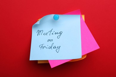 Paper note with words Meeting on Friday pinned to red background