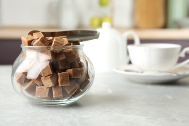 Photo of Glass bowl with brown sugar cubes and tongs on grey table