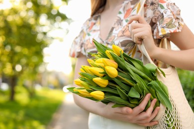 Teenage girl with bouquet of yellow tulips in park on sunny day, closeup. Space for text