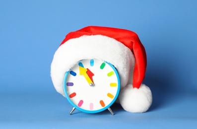 Alarm clock with Santa hat on blue background. New Year countdown