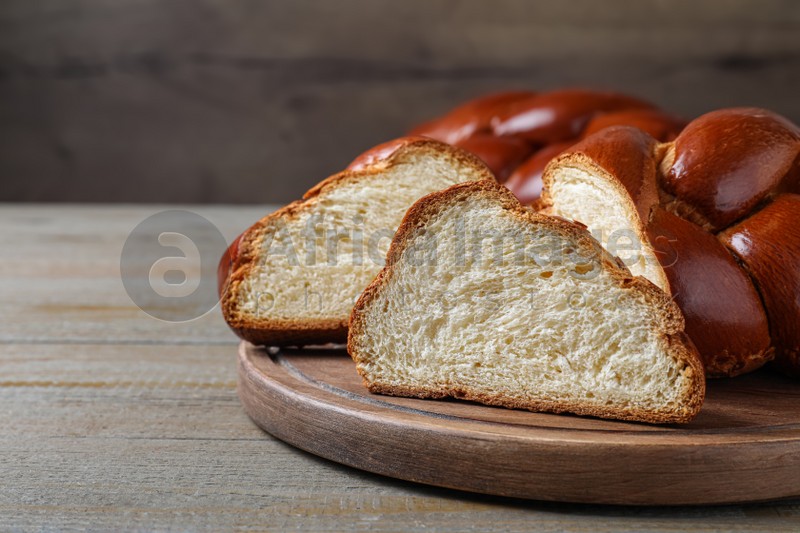 Photo of Cut homemade braided bread on wooden table, space for text. Traditional Shabbat challah