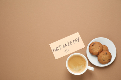 Delicious morning coffee, cookies and card with HAVE A NICE DAY wish on brown background, flat lay. Space for text