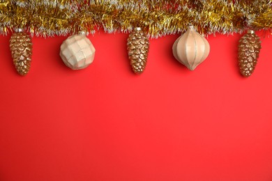 Shiny golden tinsel and Christmas baubles on red background, flat lay. Space for text