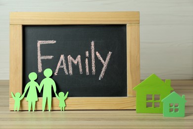 Photo of Happy Family Day. Blackboard, paper parents and their children near house models on wooden table