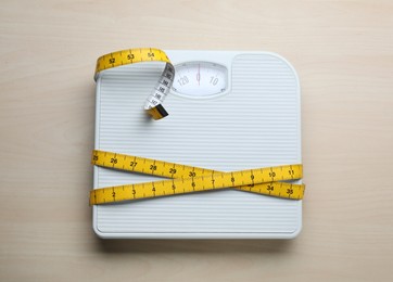 White bathroom scale and measuring tape on wooden floor, top view. Weight loss concept