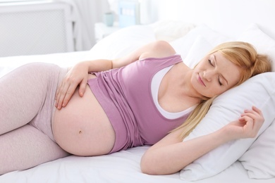 Young pregnant woman sleeping on bed in light room