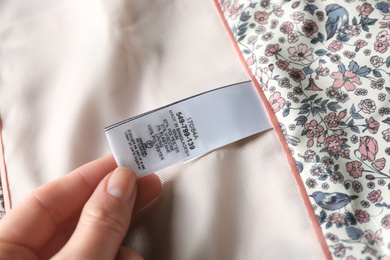 Photo of Woman reading clothing label with size and content information on light garment, closeup