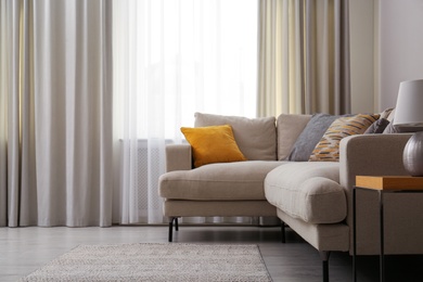 Modern comfortable sofa near window in stylish living room. Interior design