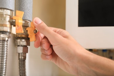 Photo of Man turning on valve of gas boiler indoors, closeup
