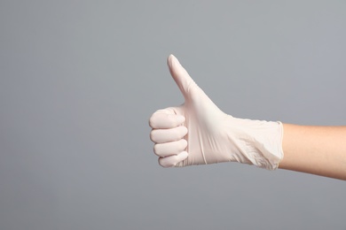 Doctor in medical gloves showing thumb up on grey background, closeup. Space for text