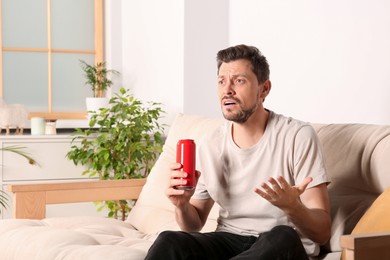 Disappointed man with can of beverage on sofa indoors
