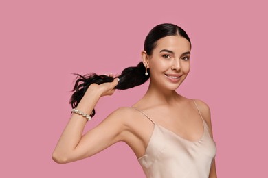 Young woman wearing elegant pearl jewelry on pink background