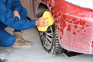 Young worker cleaning automobile wheel at car wash, closeup
