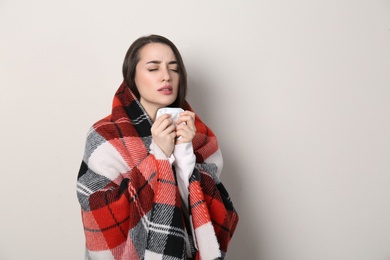 Young woman with blanket suffering from runny nose on beige background. Space for text