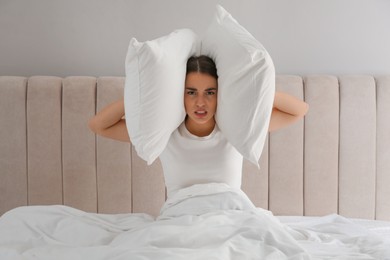 Unhappy young woman covering ears with pillows in bed at home. Noisy neighbours